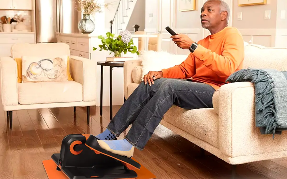 An old man is using a Tousains mini elliptical machine while watching TV.